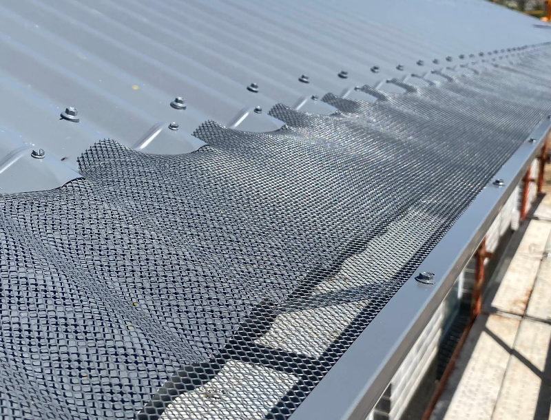 A close up of a gutter with a roof in the background.