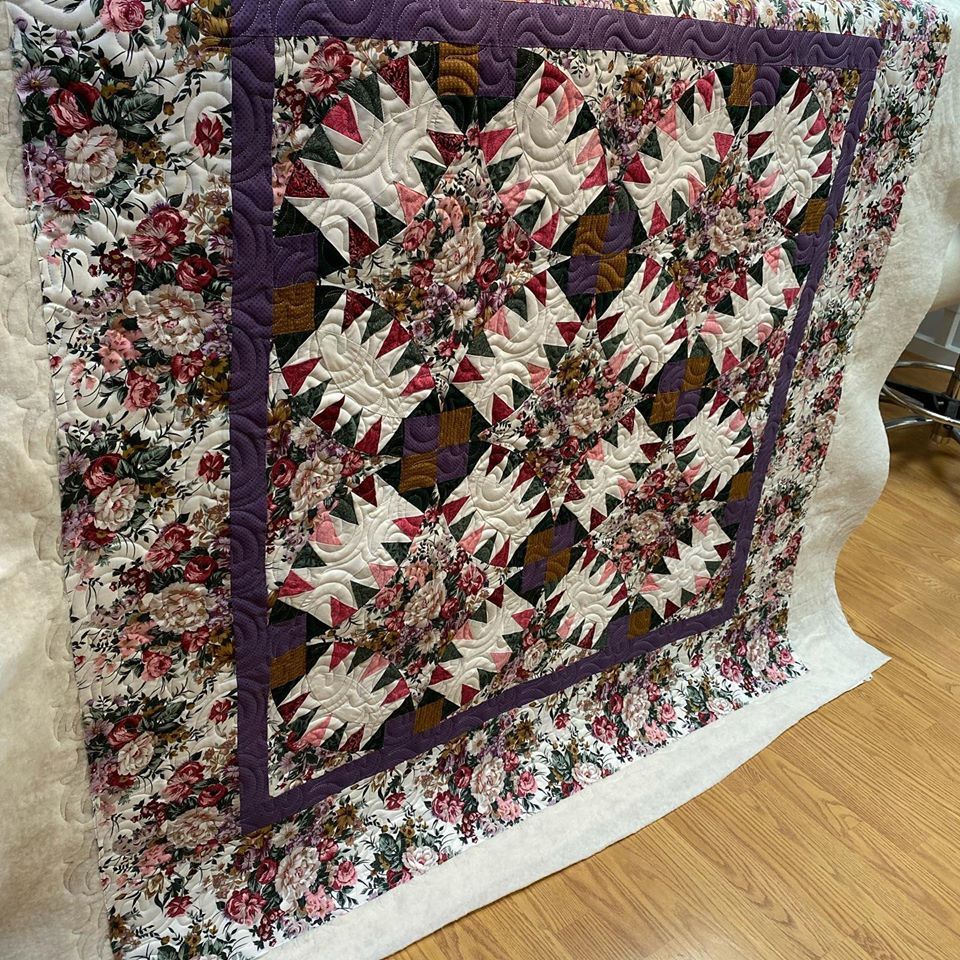 A quilt with a purple border is sitting on a wooden floor.
