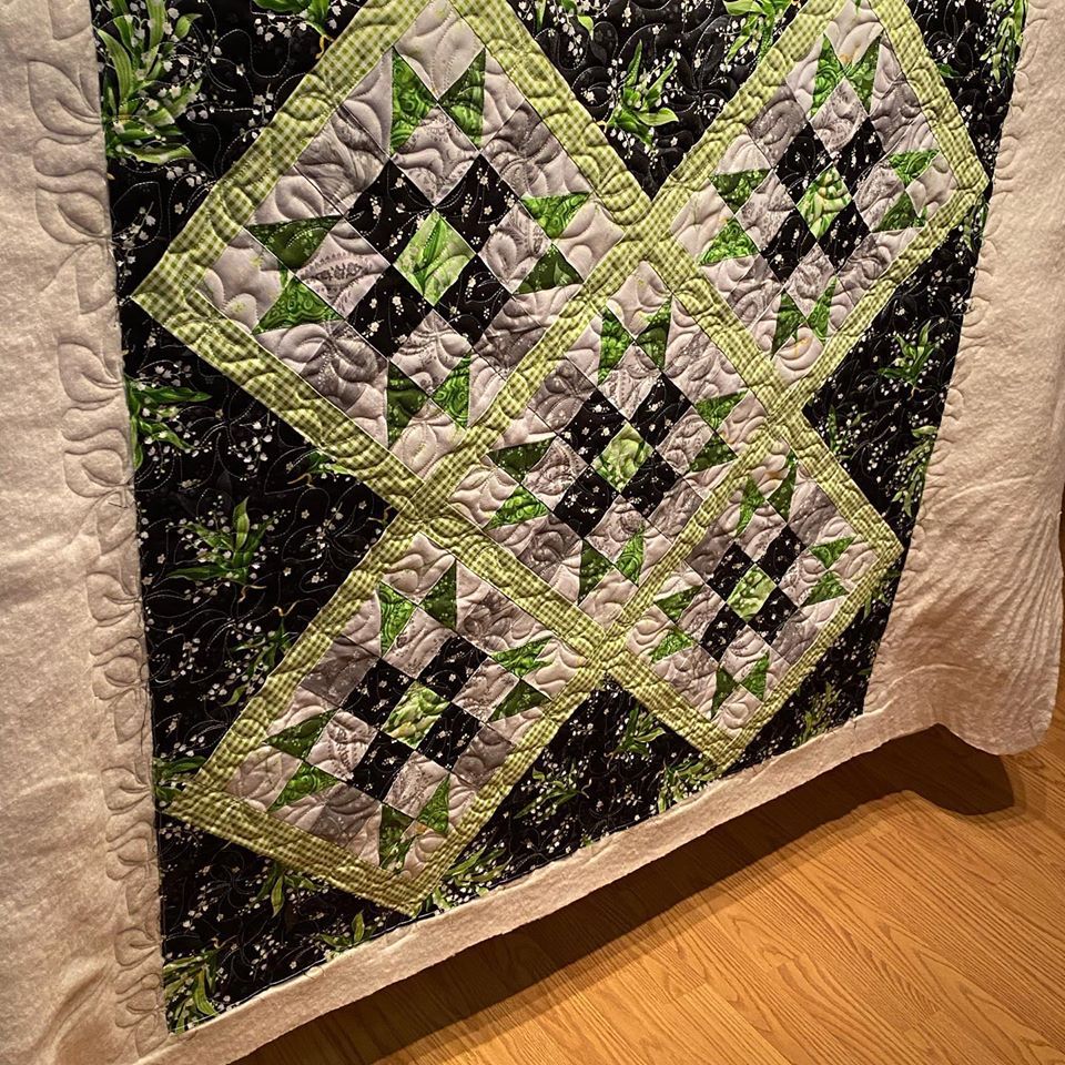 A black and green quilt is sitting on a wooden floor.