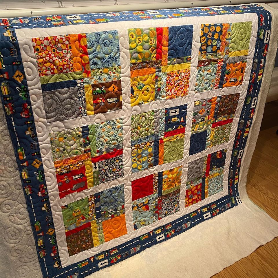 A colorful quilt with a blue border has the letter b on it