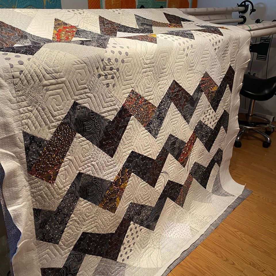A quilt with a chevron pattern is sitting on a wooden floor.