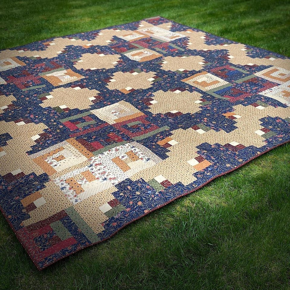 A large quilt is sitting on top of a lush green field.