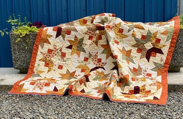 A quilt is sitting on the ground in front of a blue wall.