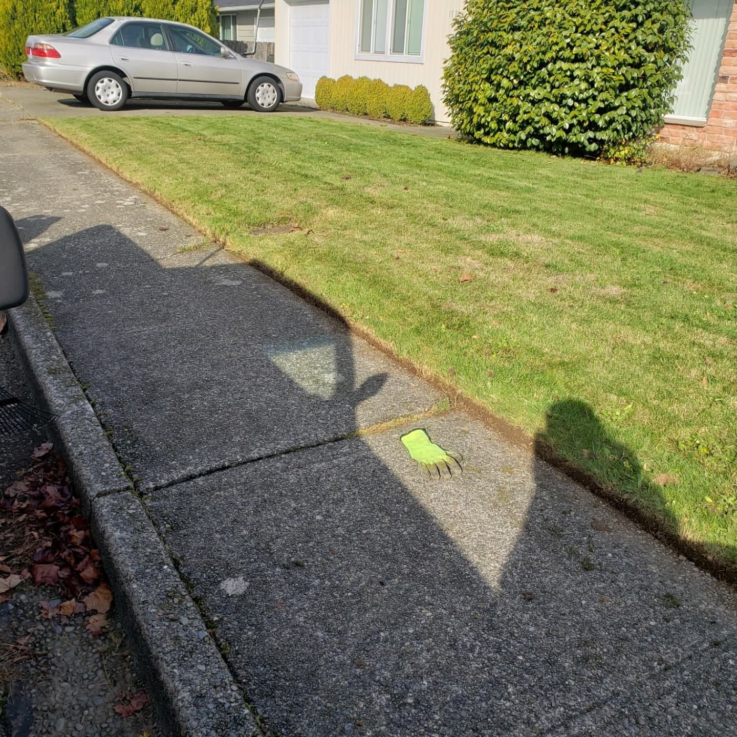 Sidewalk with grass and parked car. Green glove on the concrete. Shadow from above. Sidewalk with grass and parked car. Green glove on the concrete. Shadow from above.