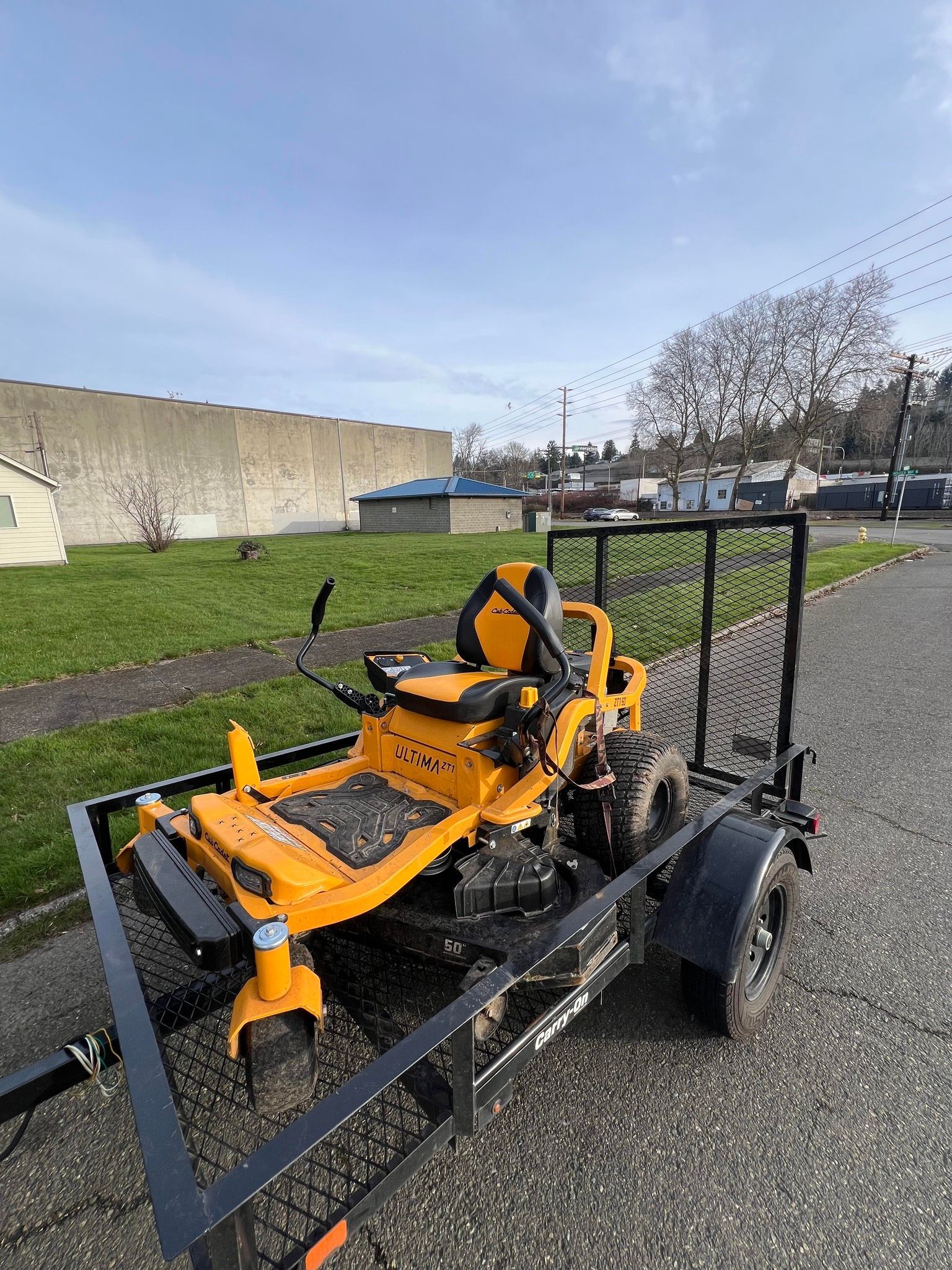 Yellow Cub Cadet zero-turn mower on a black trailer, parked outdoors. Yellow Cub Cadet zero-turn mower on a black trailer, parked outdoors.