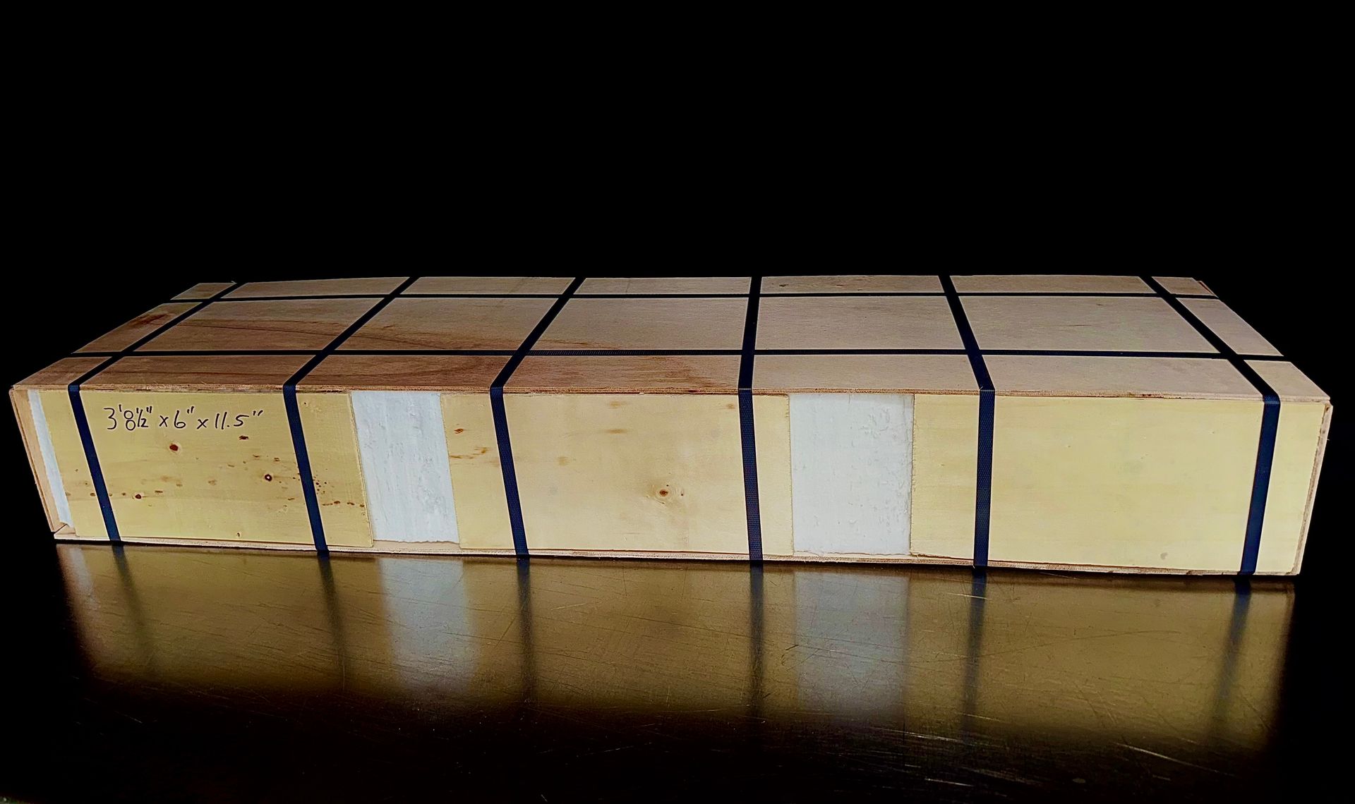 Tan rectangular box with black tape grid, white labels, on reflective black surface.