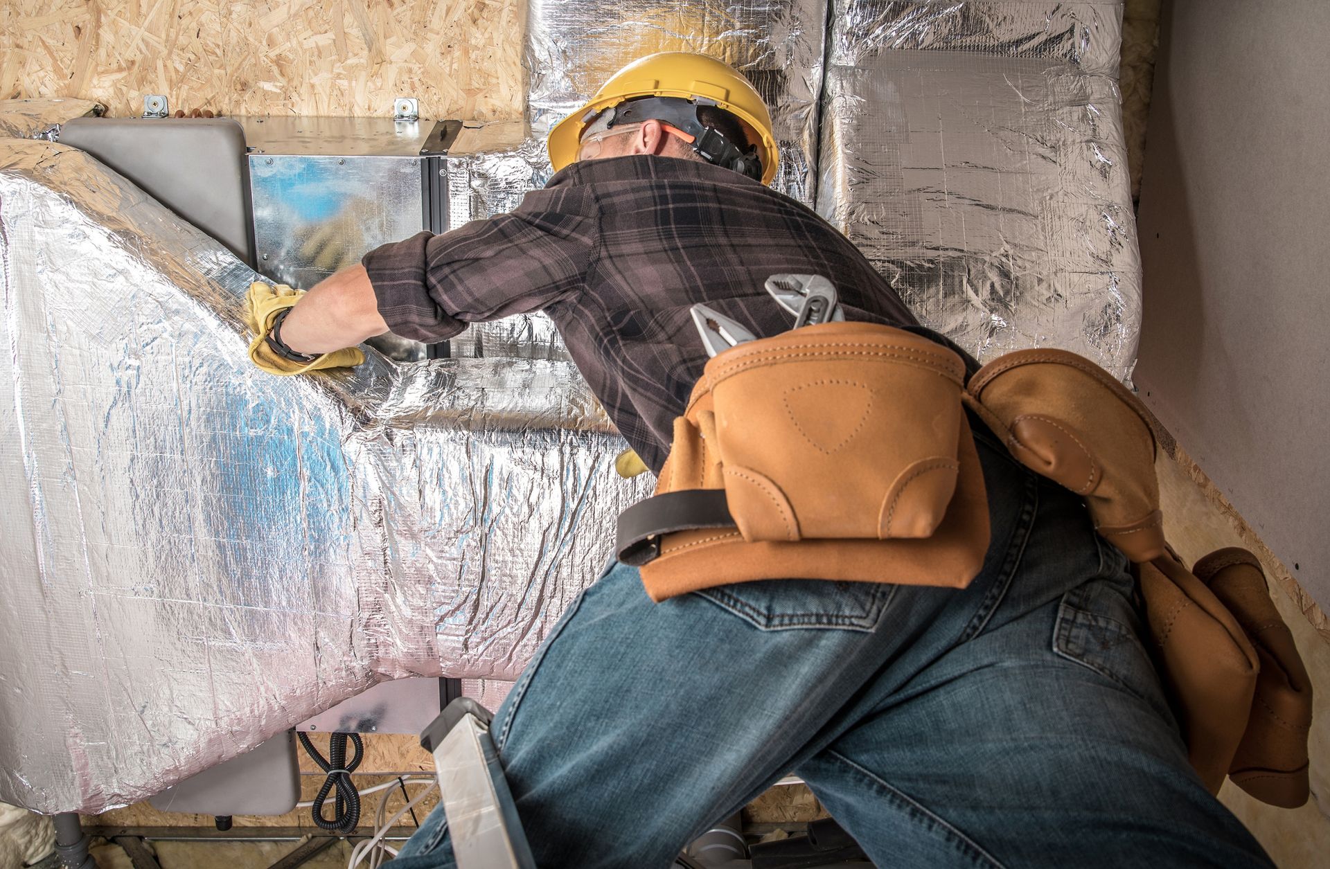 A worker in a yellow hard hat installing a furnace and central heating pump duct.