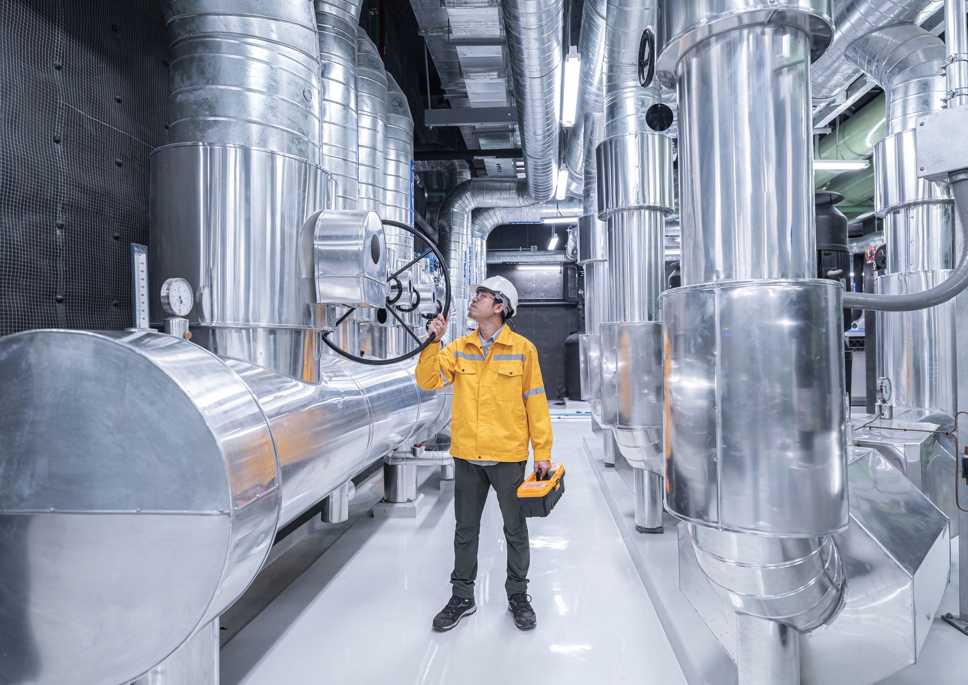 An engineer with a toolbox working on equipment at an oil and gas factory, operating a pipeline.