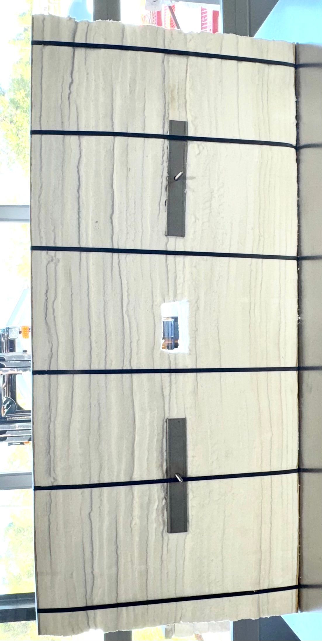 Close-up of a light-colored wooden wall with horizontal black lines and dark rectangles.