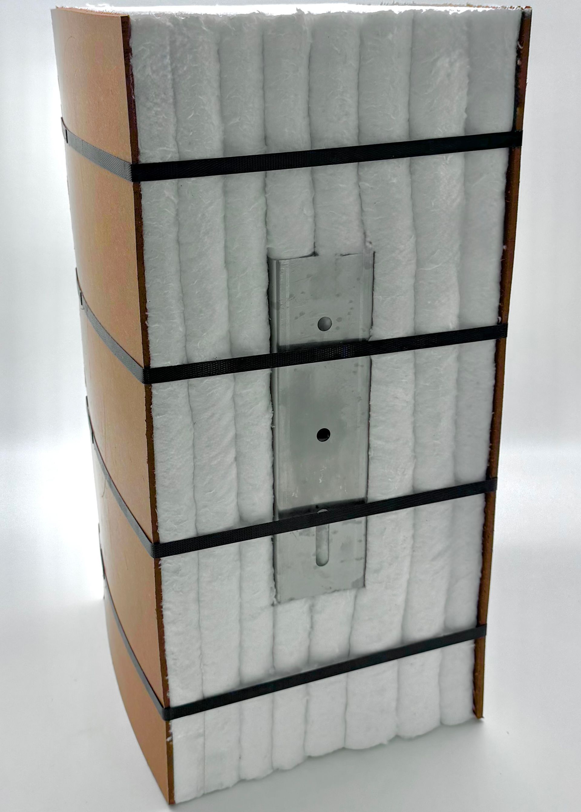 A rectangular composite object: wood, white insulation, metal plate, and black straps.