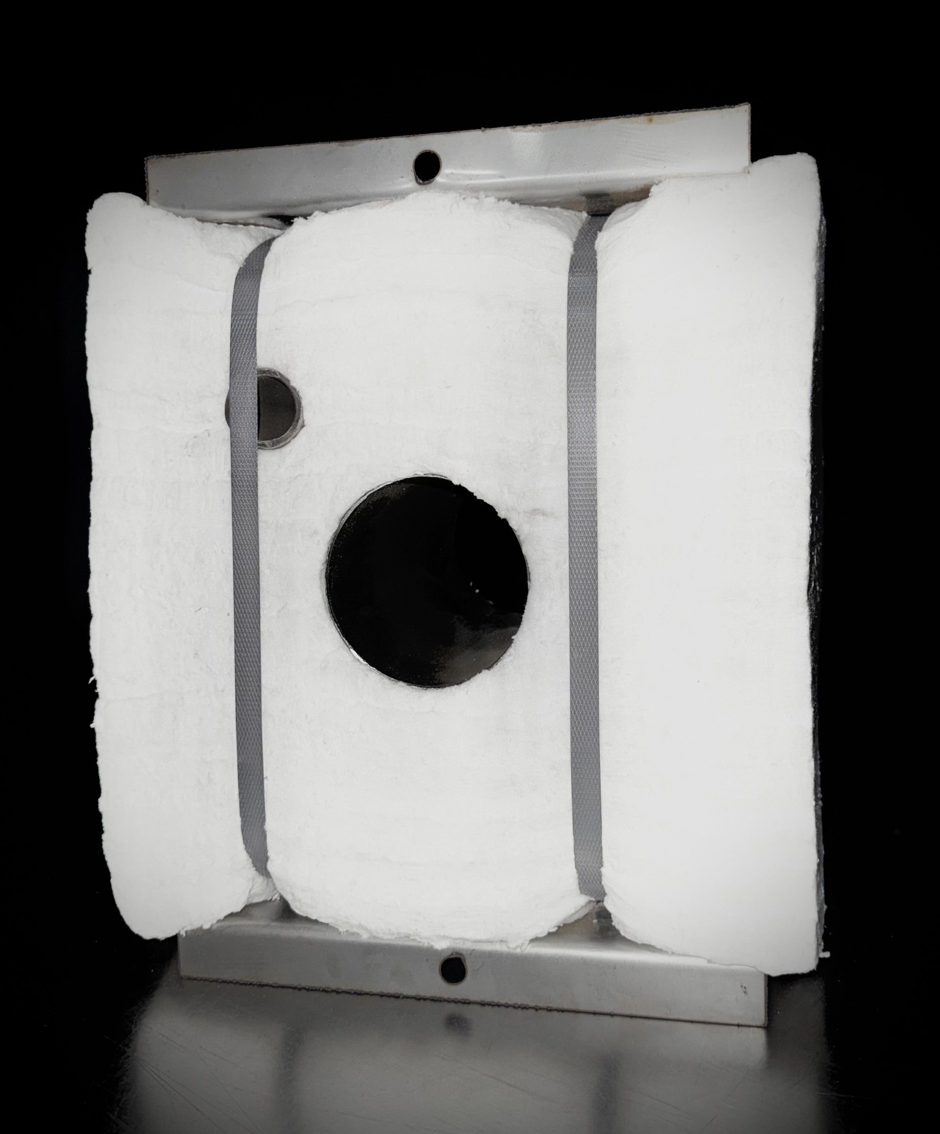 White, rectangular soundproofing panel with a central black hole, held in a silver frame against a black background.