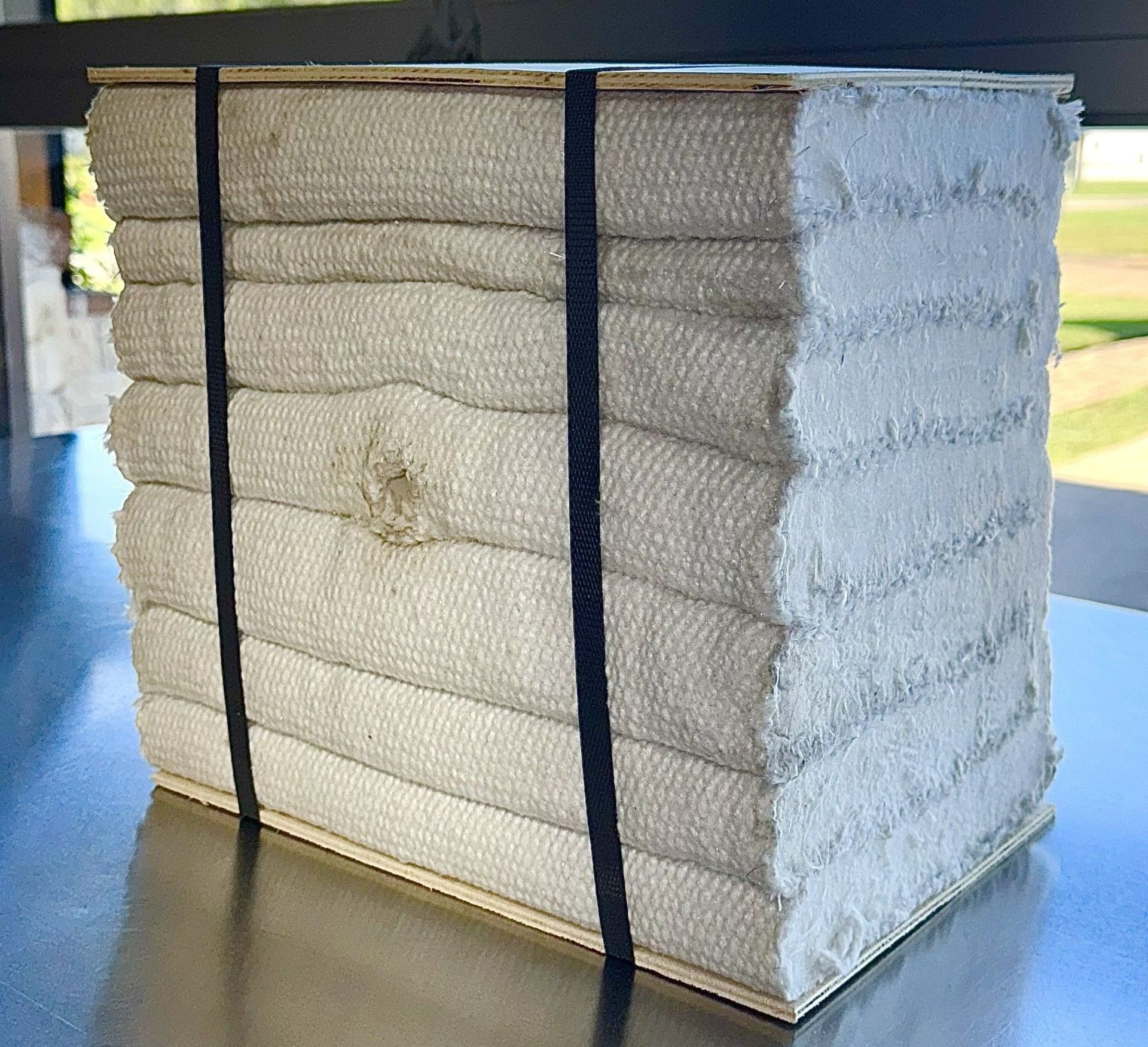 Bundle of white, folded textiles secured by black straps, set on a stainless steel surface.