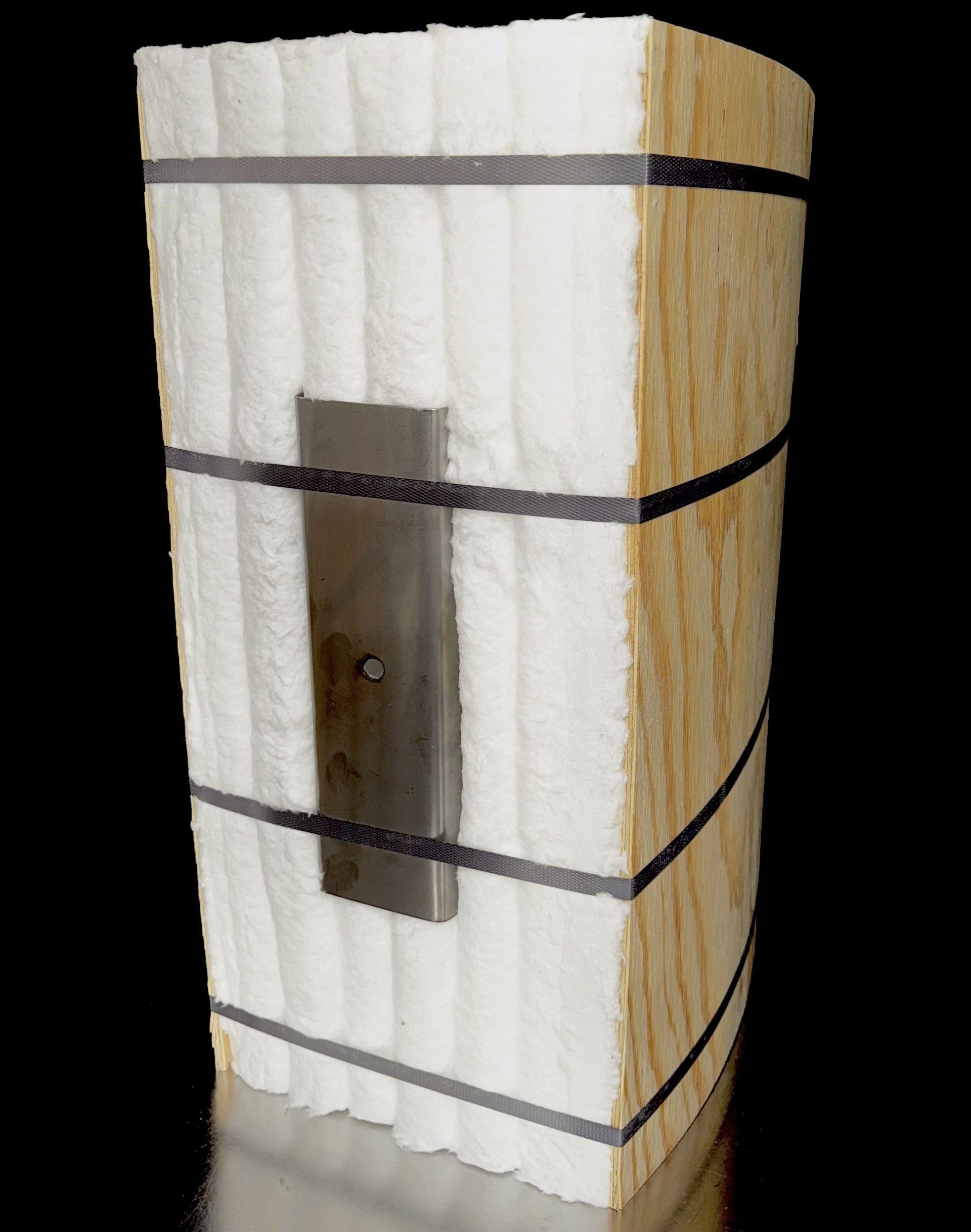 A rectangular composite object: wood, white insulation, metal plate, and black straps.