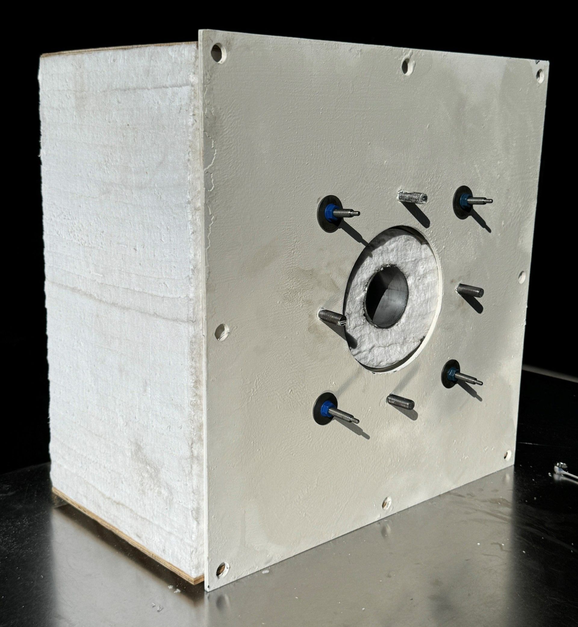 White cube with a metal faceplate, a central hole, and protruding metal pins.
