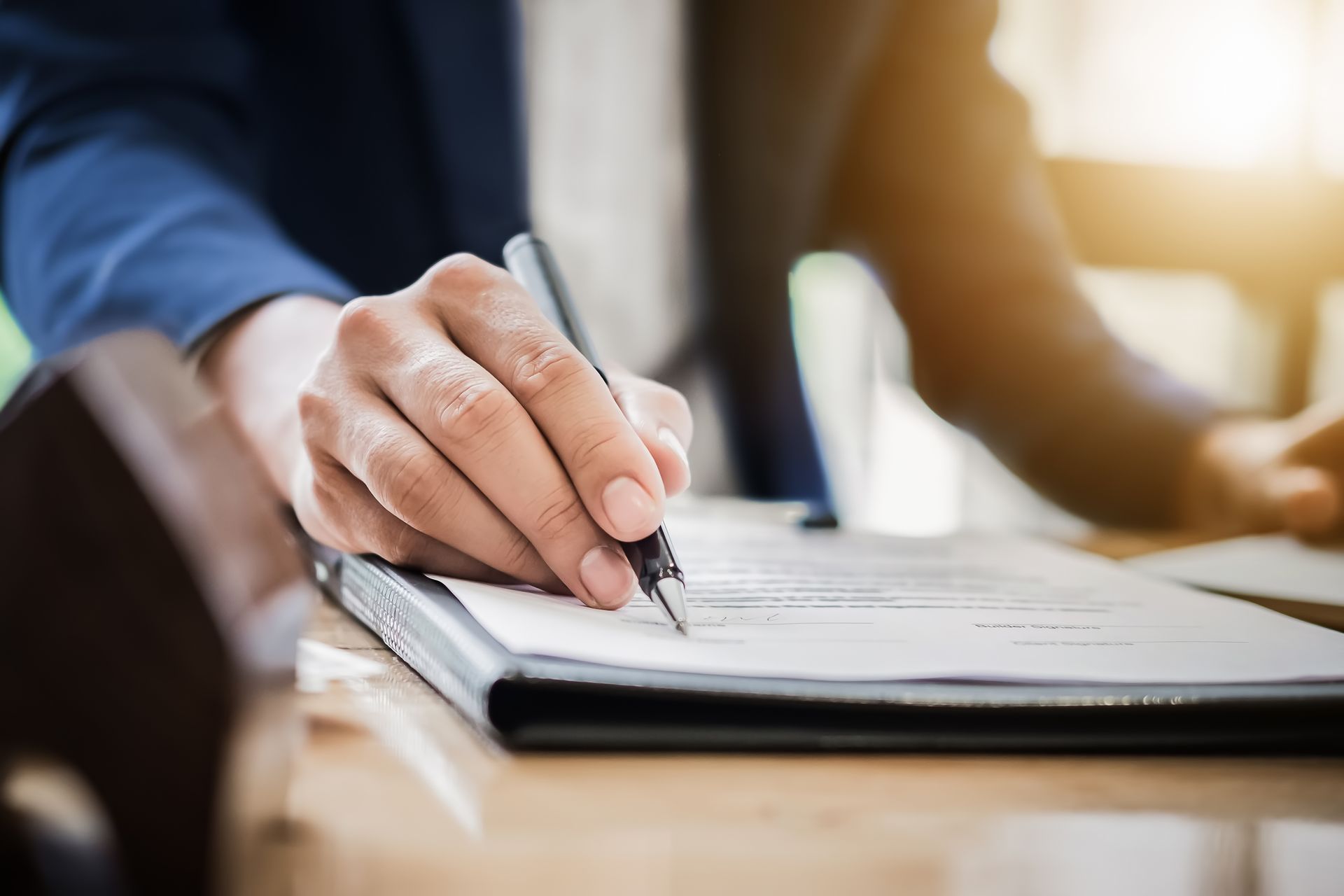 Hand writing notes in a notebook at a desk with a pen.