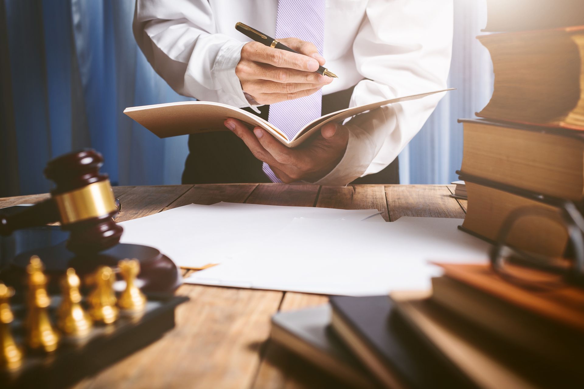 Lawyer taking notes in an open book beside a gavel and stacked books on a desk.