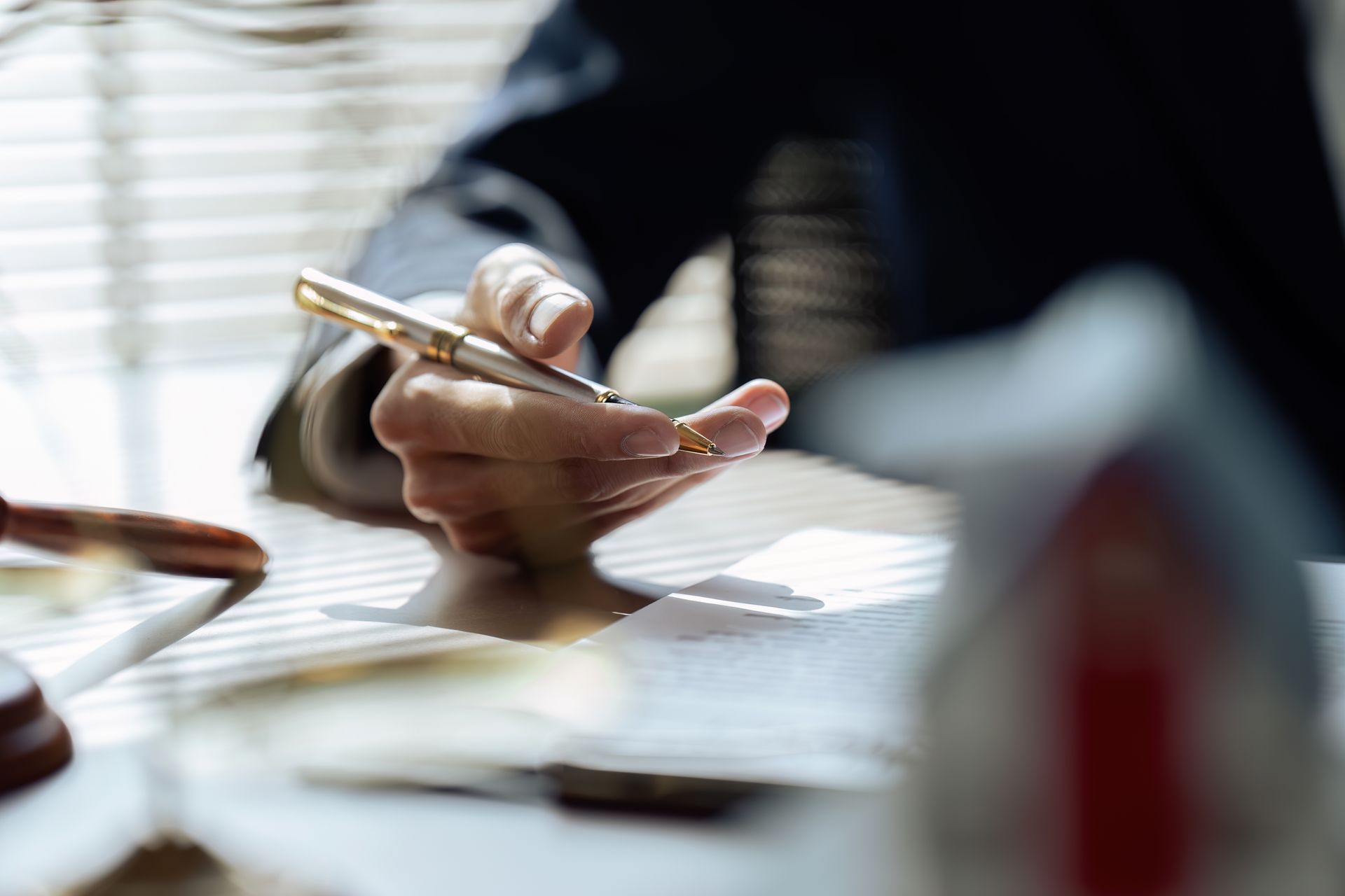 Person writing with a gold pen at a desk beside a laptop and papers