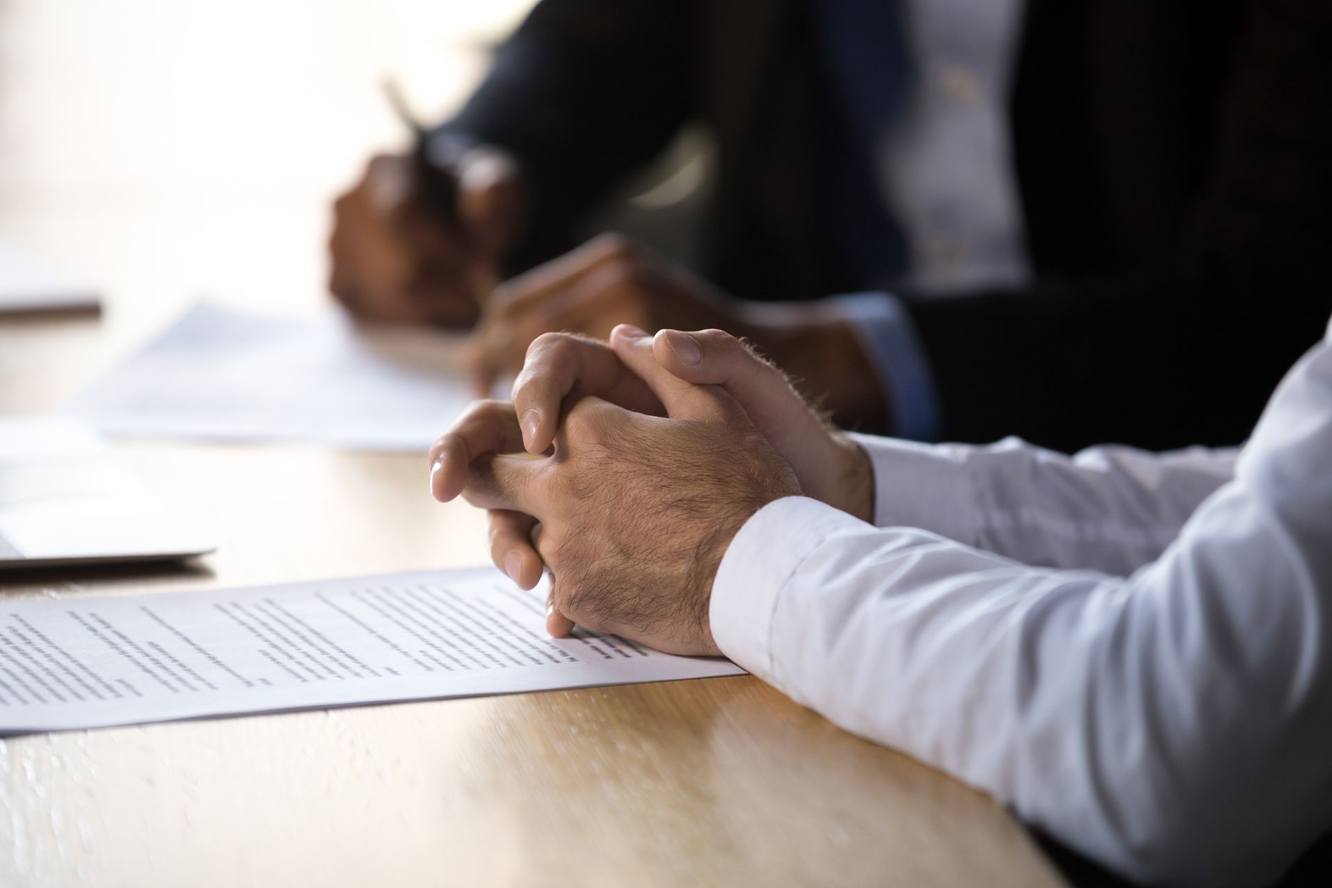 Hands clasped over documents on a meeting table.