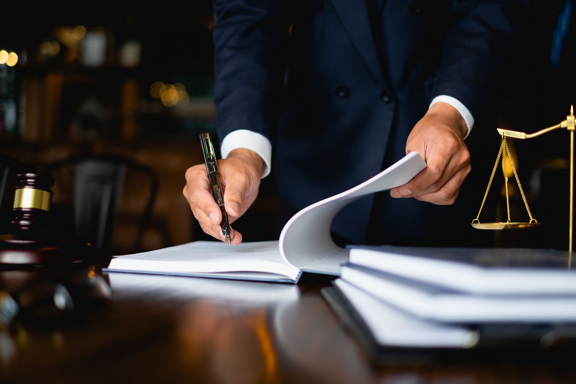 Lawyer signing documents at a desk with a gavel and scales of justice in view.