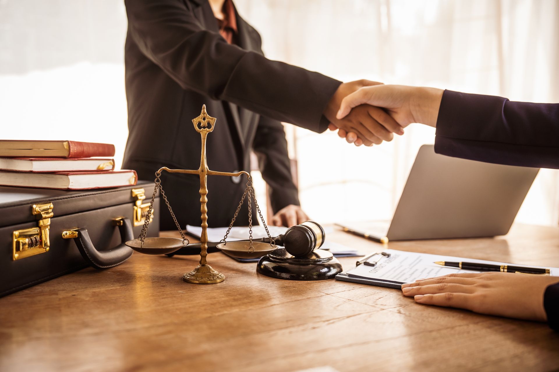 Two people shaking hands across a desk with a scale of justice.