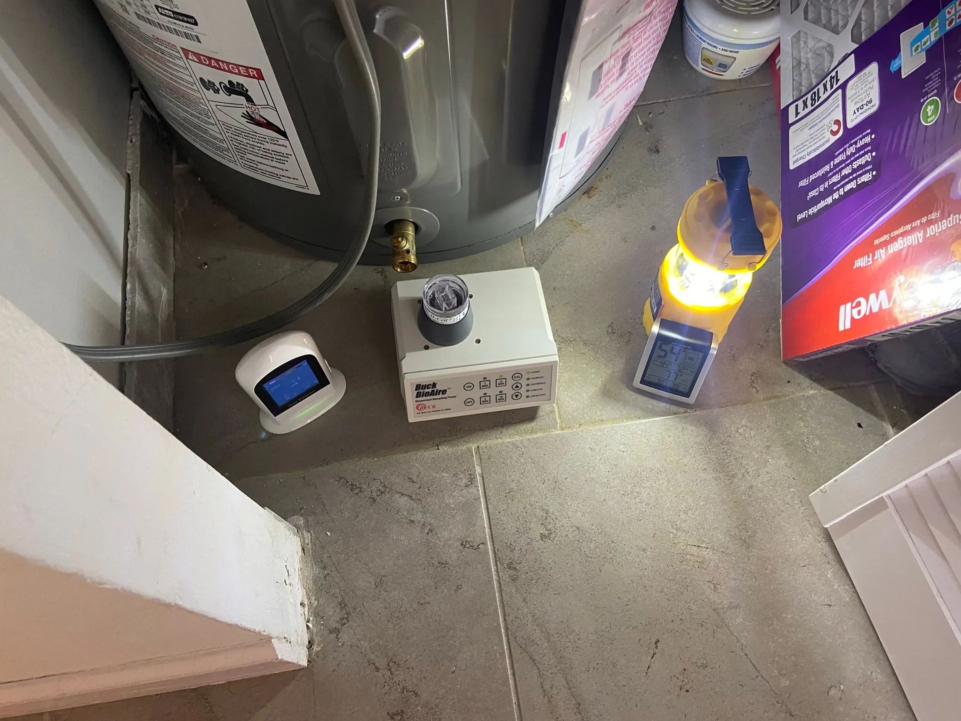 A water heater, control panel, and flashlight sit on a concrete floor next to a wall.