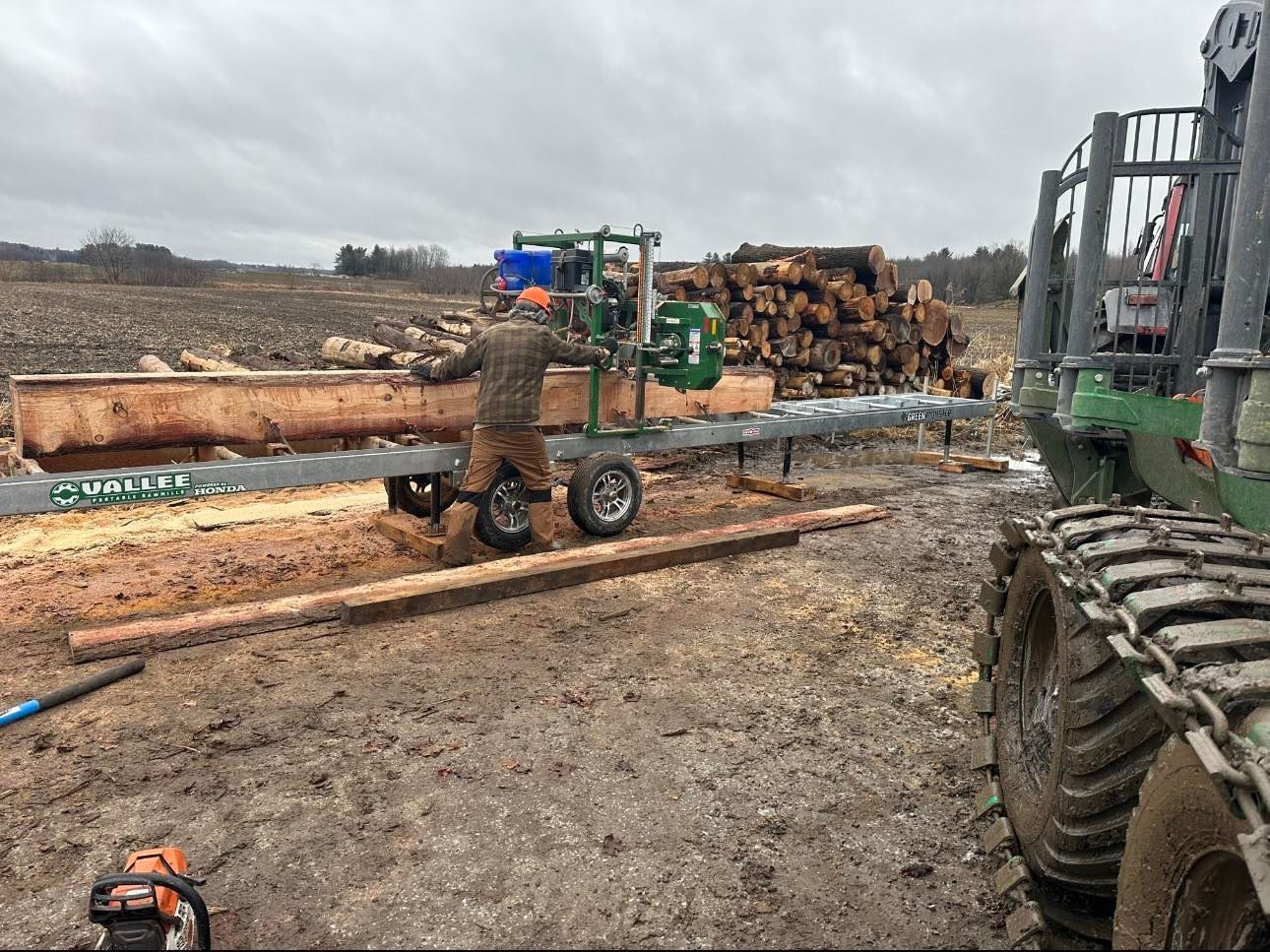 Un homme utilise une tronçonneuse pour couper des bûches dans un champ.