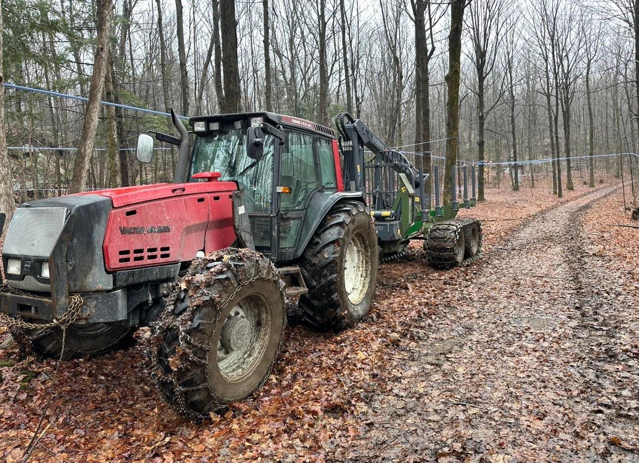 Un tracteur rouge et noir roule sur un chemin de terre dans les bois.