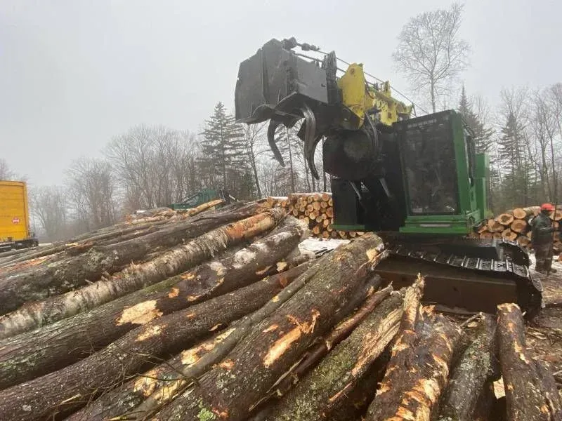 Une pile de grumes avec un tracteur en arrière-plan.