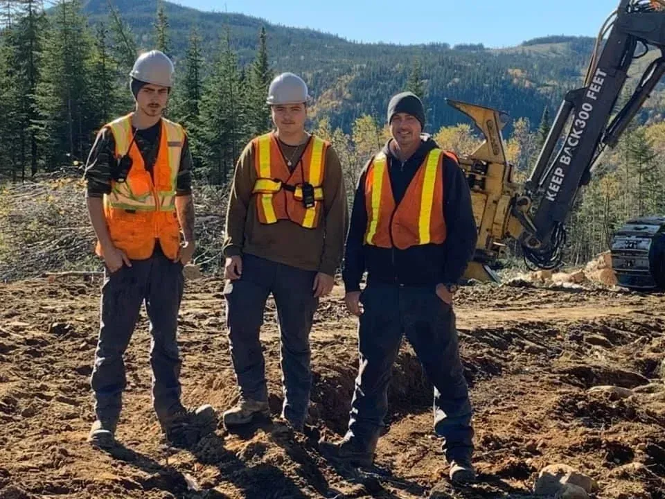 Trois ouvriers du bâtiment posent pour une photo devant une pelle Volvo