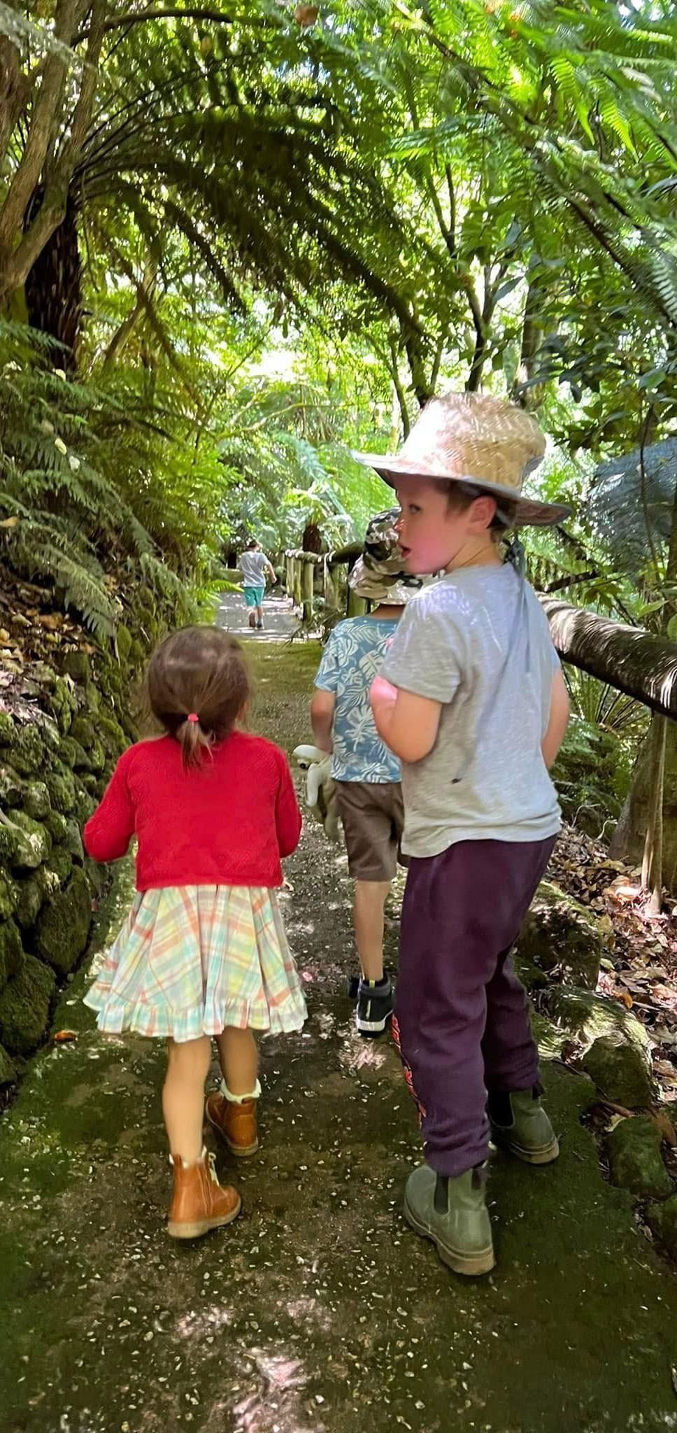 A boy and a girl are walking down a path in the woods.