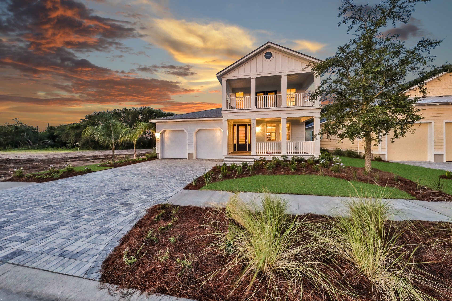 A large white house with a large driveway and a sunset in the background.