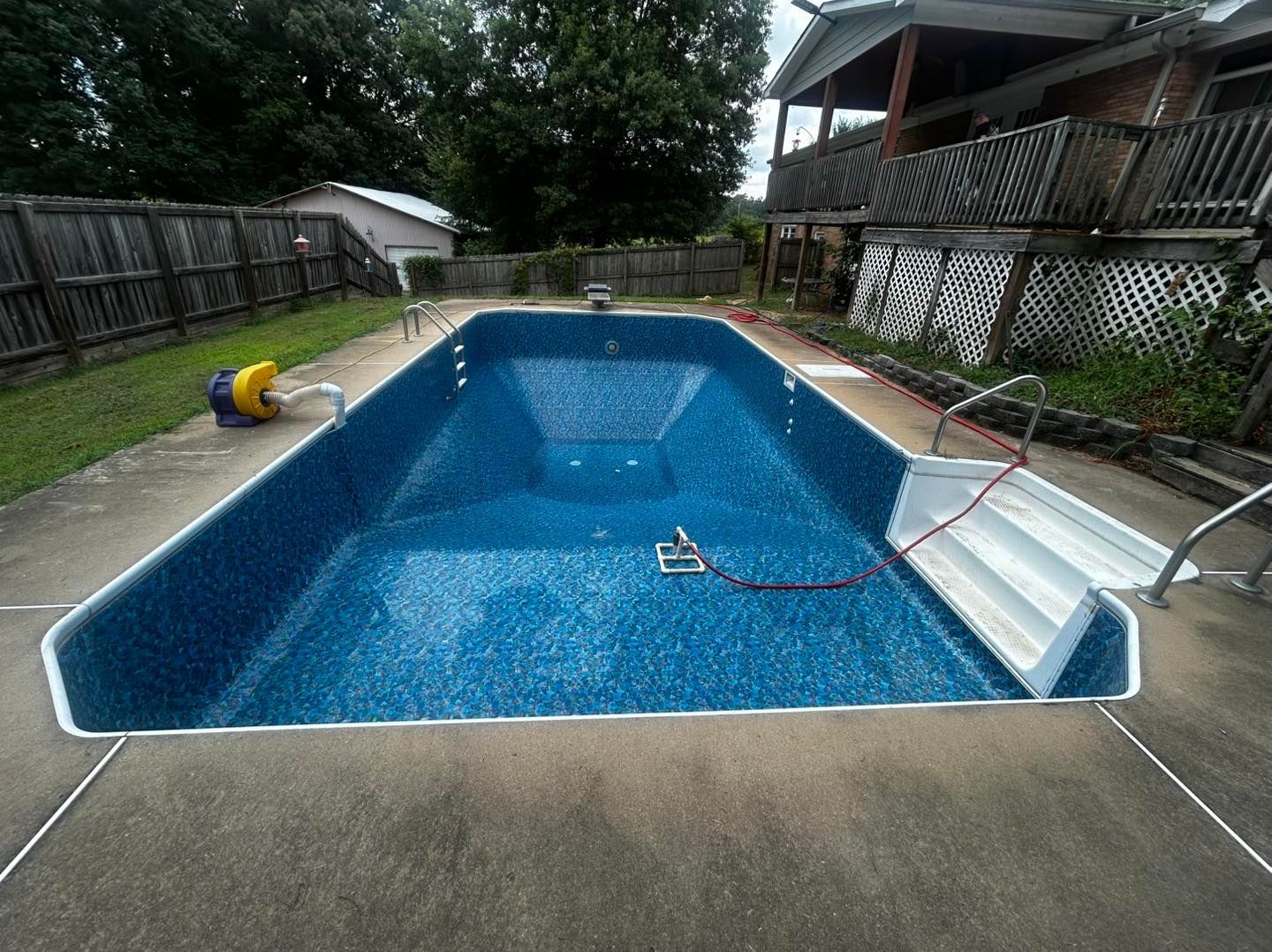 Empty rectangular swimming pool with a patterned blue liner, white built-in steps, and a concrete patio in a backyard.