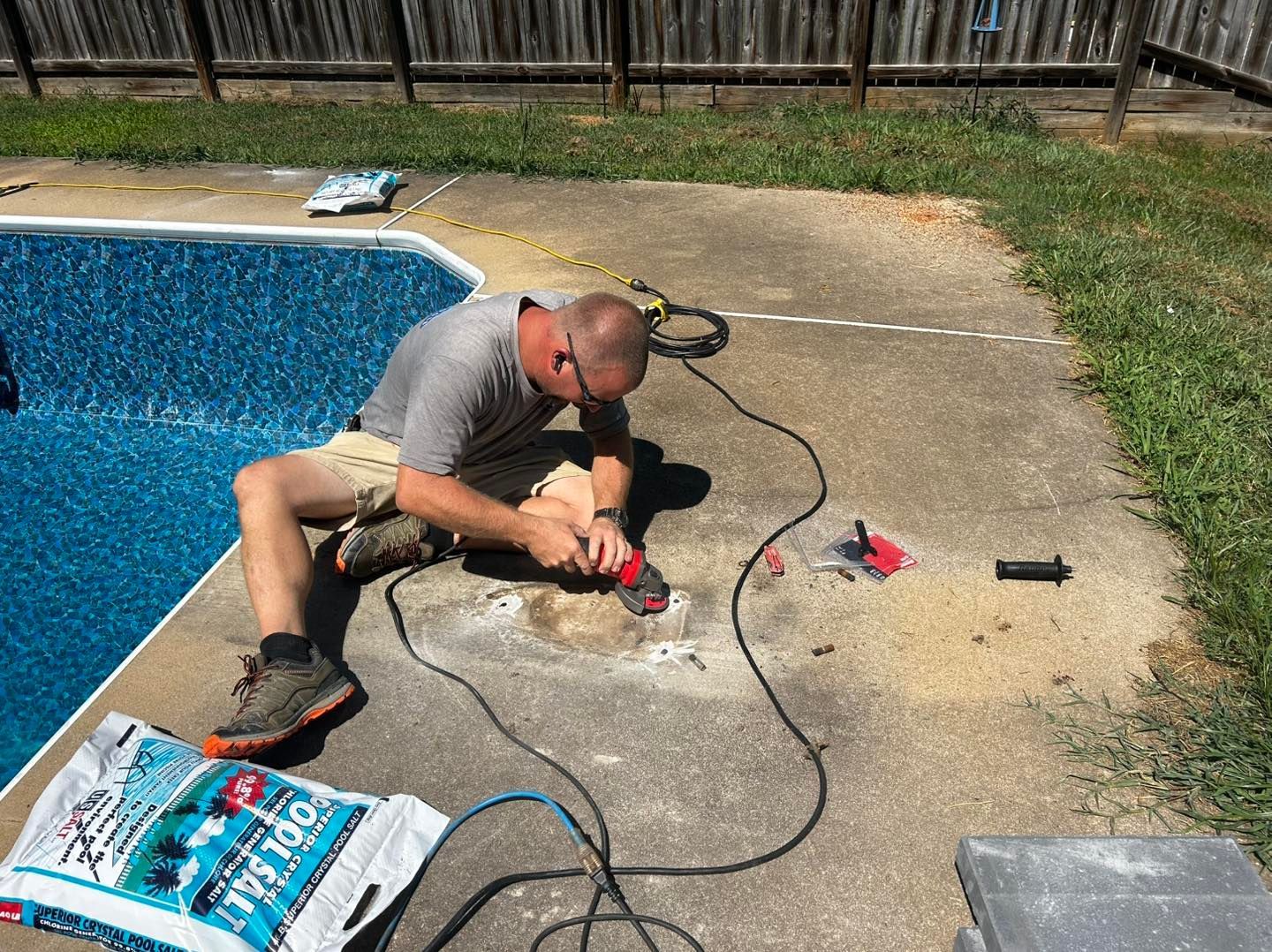 A person using a handheld power tool to repair concrete beside a swimming pool.
