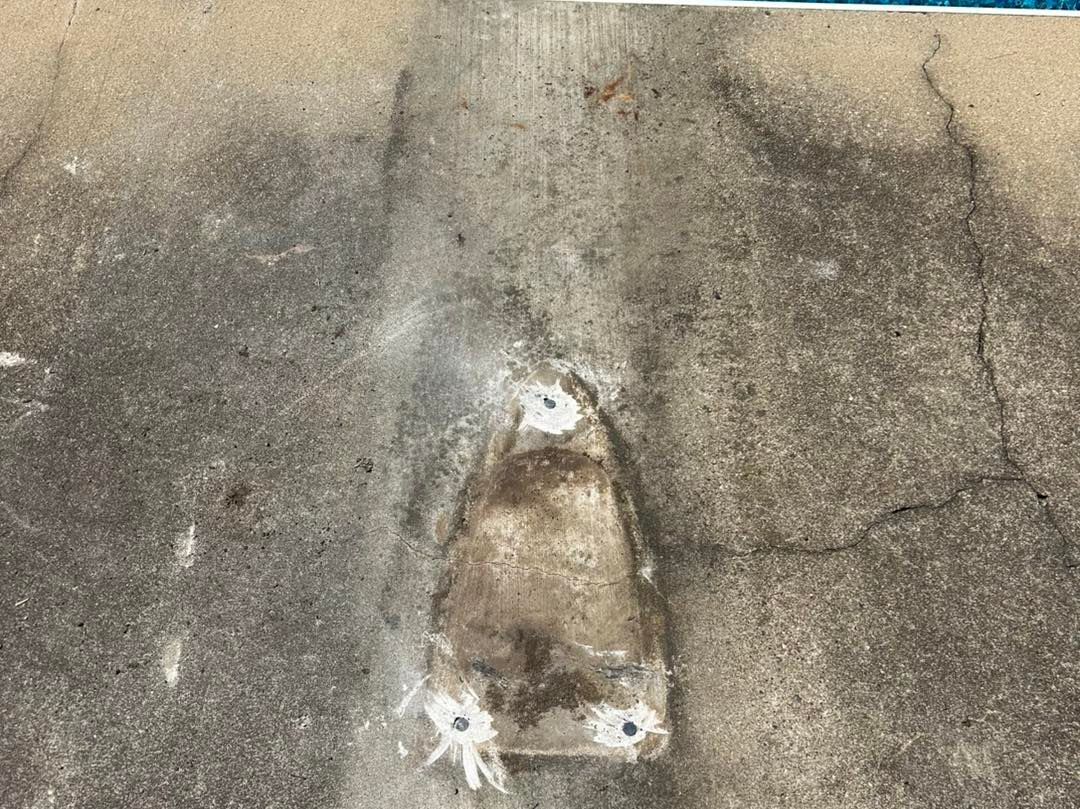 A weathered gray concrete surface featuring a triangular, recessed metal plate secured by three visible bolts.