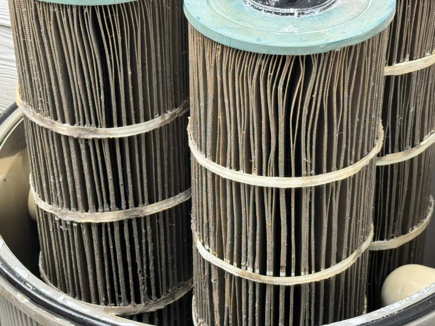 A close-up view of dirty, dark brown swimming pool filter cartridges inside a housing container.