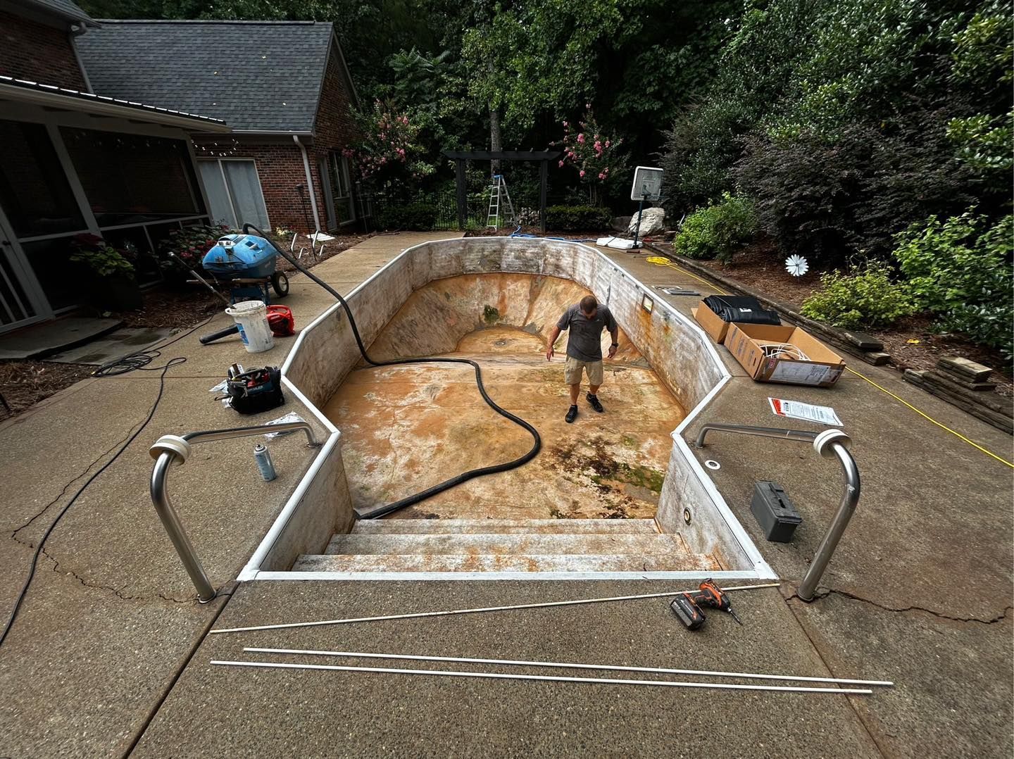 A worker stands inside an empty, rectangular, light-colored backyard swimming pool undergoing renovation.