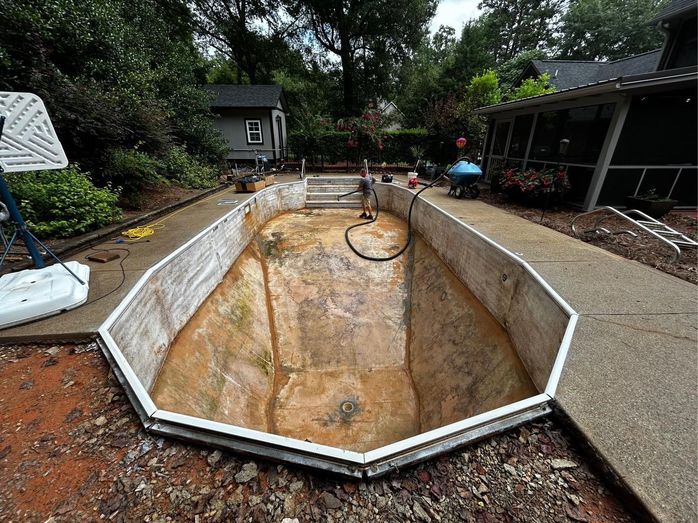 An empty, octagonal backyard swimming pool undergoing renovation, surrounded by concrete decking and dirt.