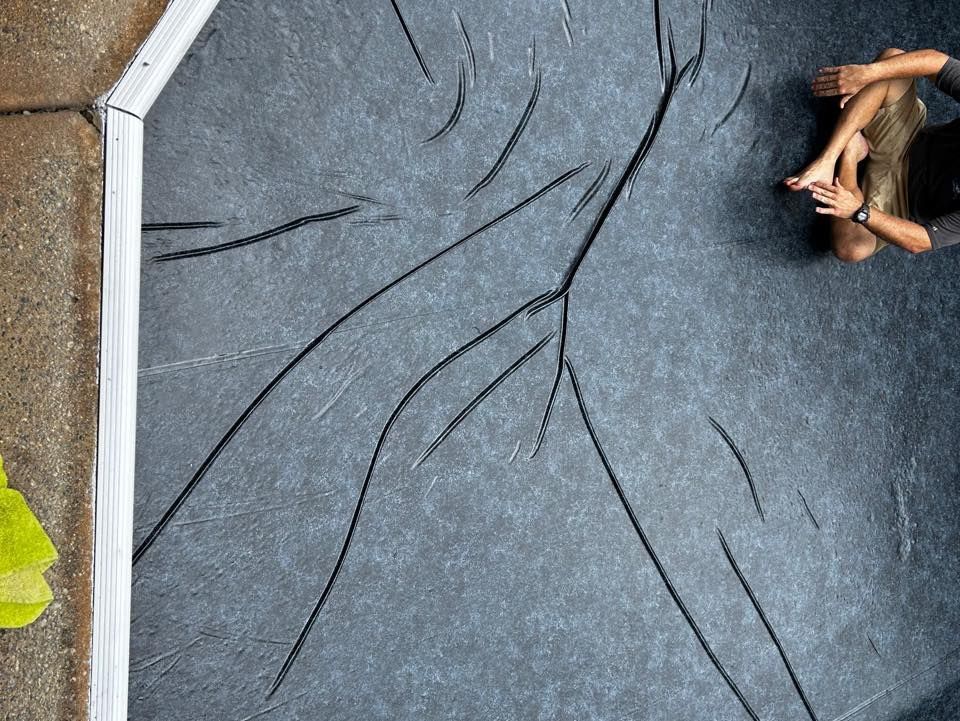 A person sits cross-legged on a dark, textured surface with prominent branching crack patterns across it.