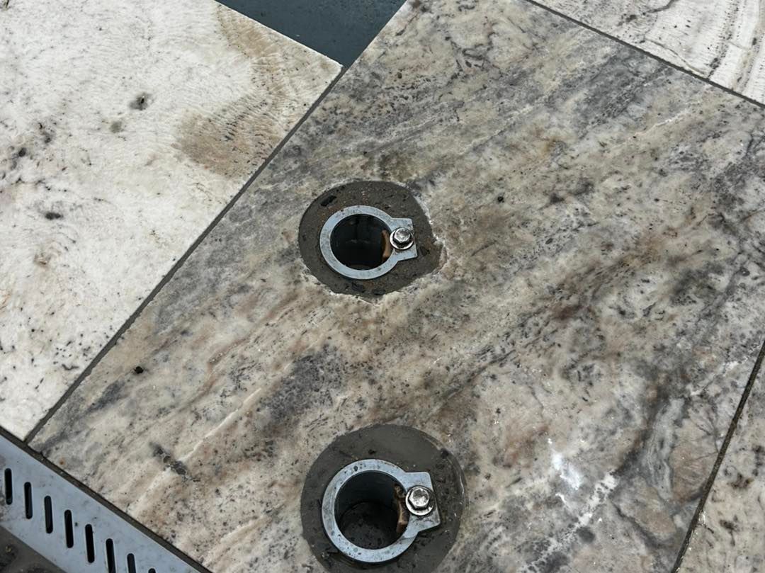 Two metal floor-mounted stanchion base plates set into light-colored stone tiles.