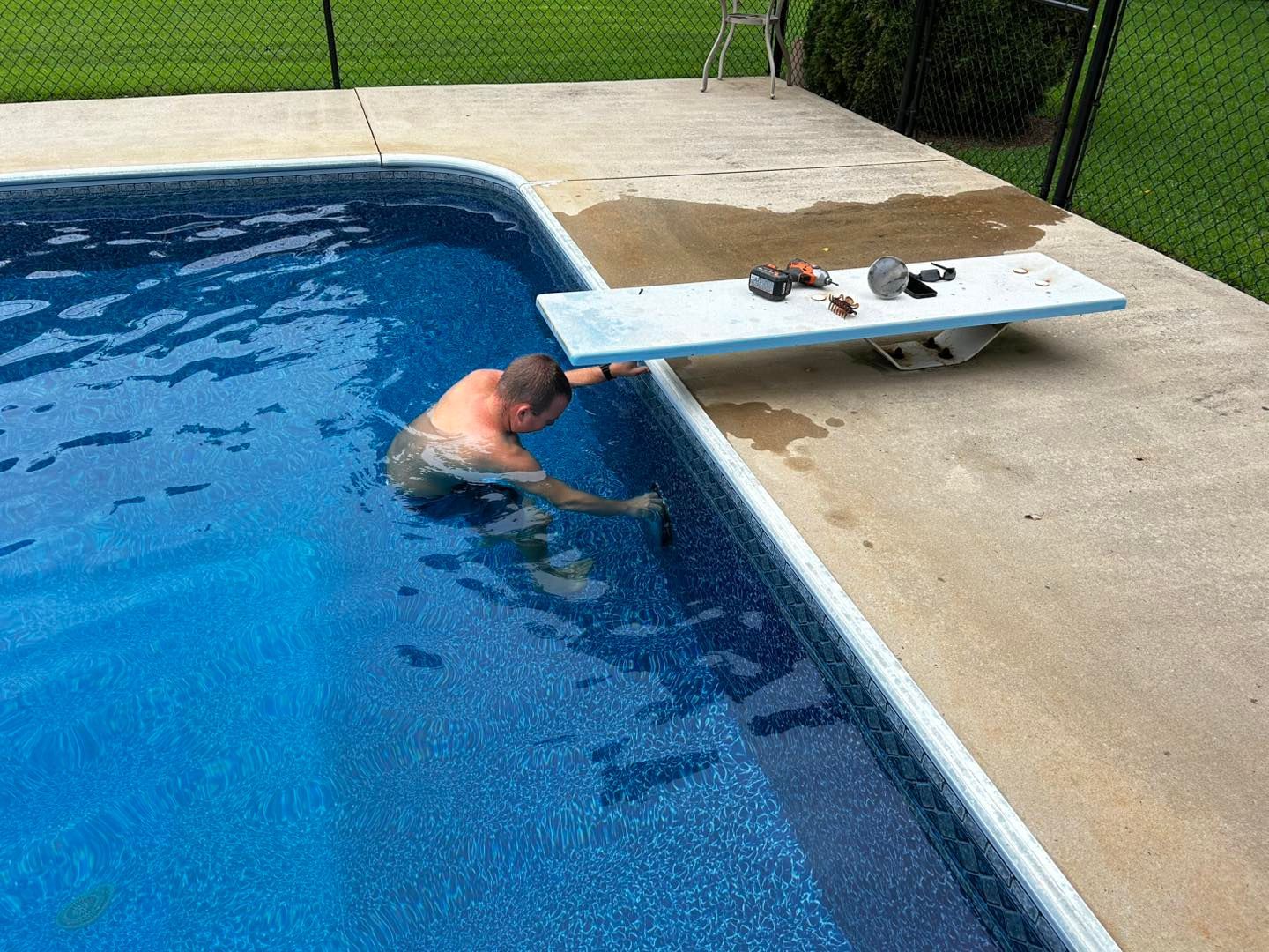 A person works on a pool diving board while partially submerged in the water.