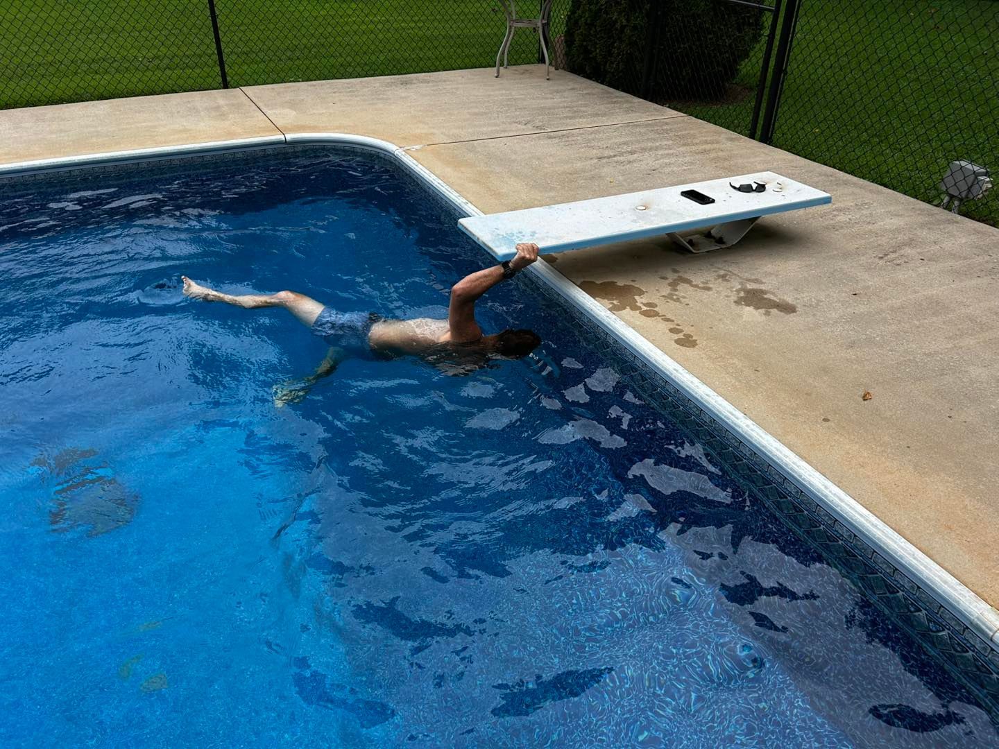 A person swims in a pool near a diving board, with one hand resting on the pool's edge.