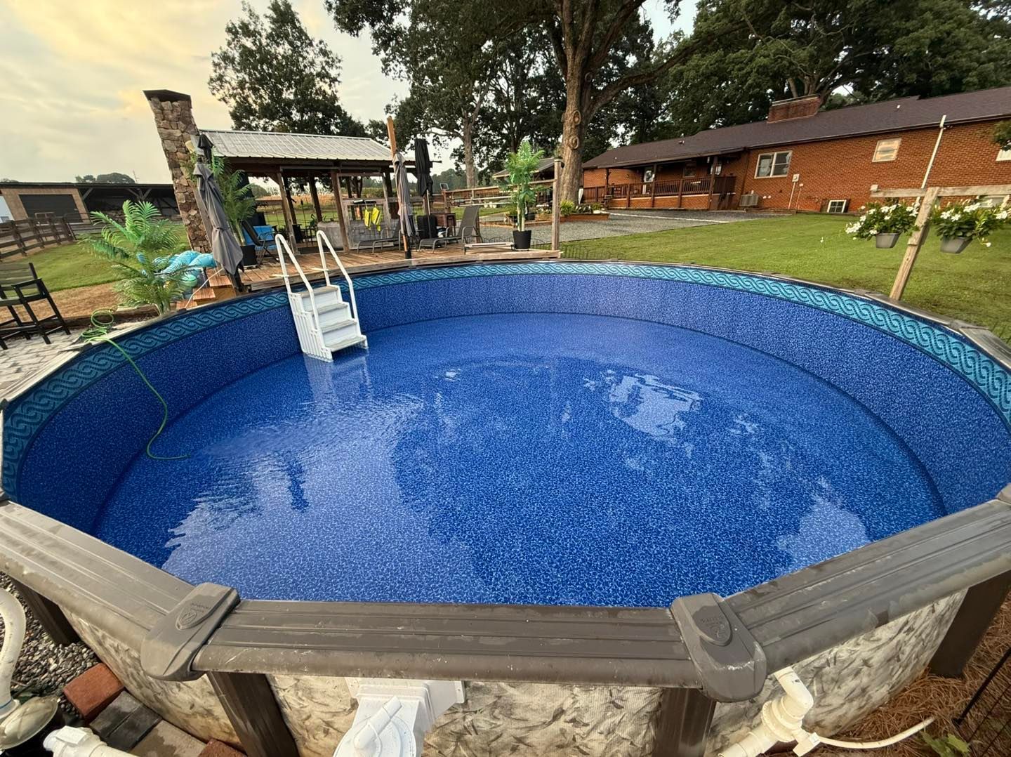 A circular above-ground pool filled with blue water, featuring a white ladder, set in a backyard near a brick house.