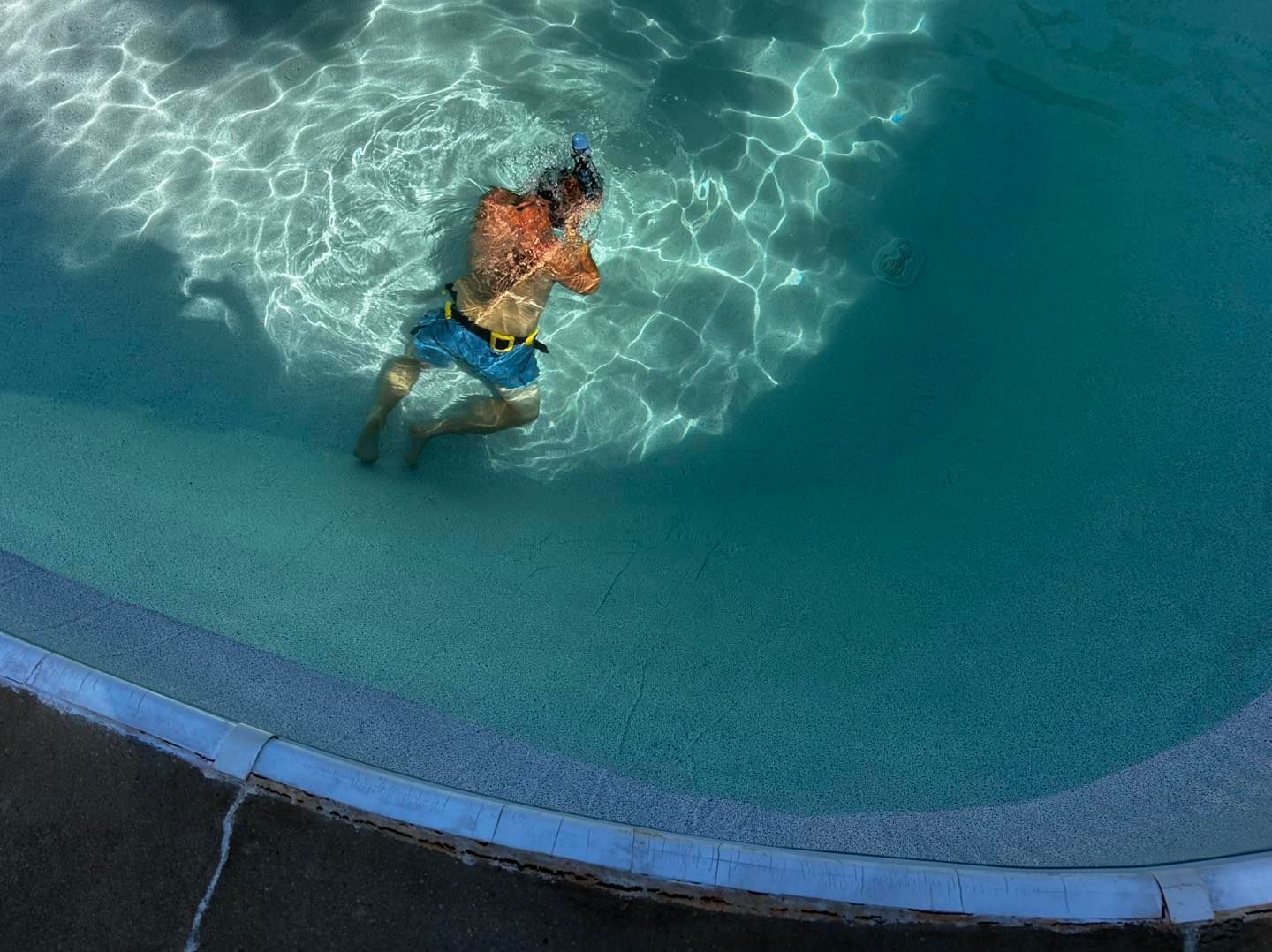 A person wearing blue swim trunks floats in a turquoise swimming pool.
