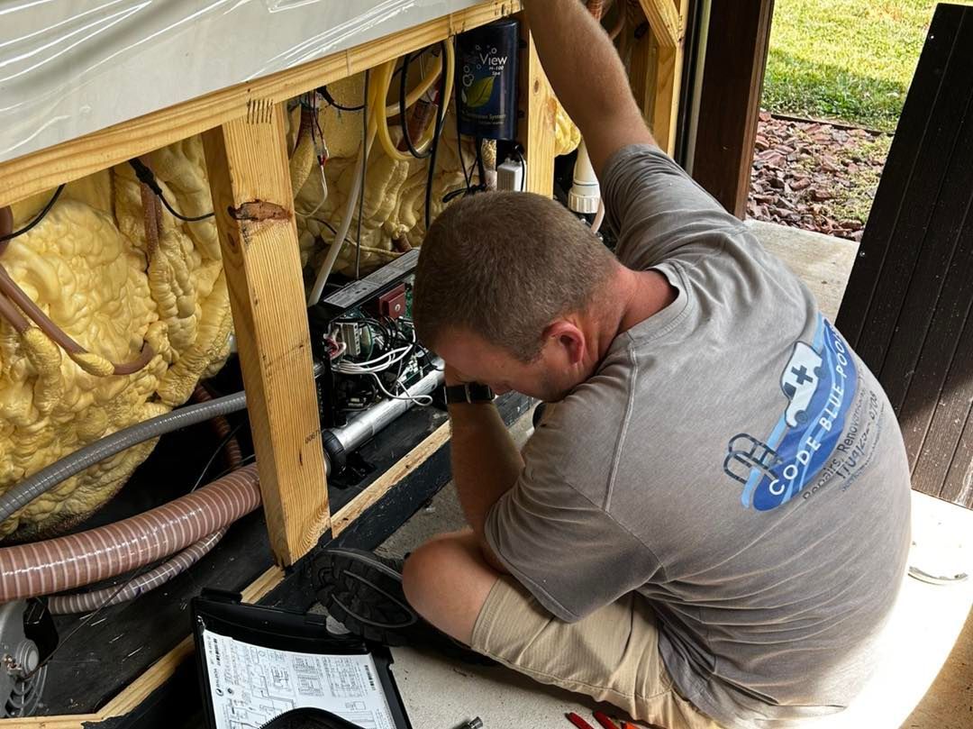 A technician repairs the mechanical components inside an open spa cabinet filled with spray foam insulation.