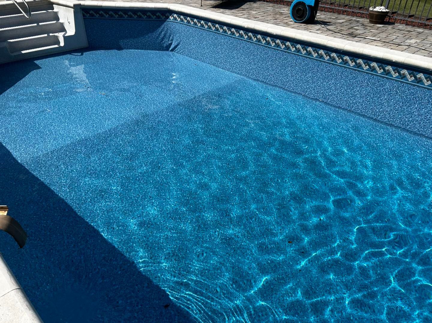 A rectangular swimming pool with a blue patterned liner and steps, viewed from the corner of a stone patio.