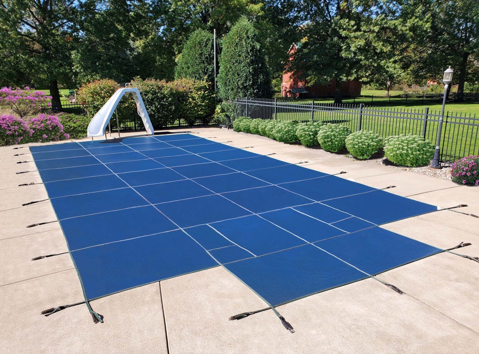 A blue rectangular pool safety cover is secured tightly over a backyard swimming pool on a sunny day.