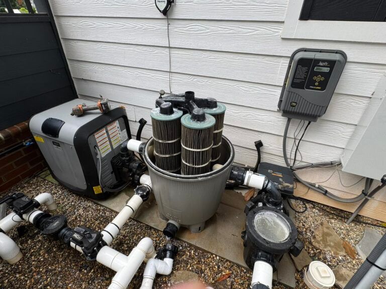 Open pool filter system with four vertical cartridge filters installed, situated outdoors against a white siding wall.