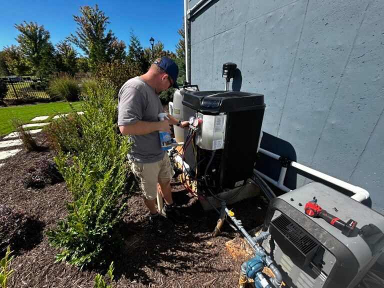 A technician in a grey shirt and cap services an outdoor HVAC or pool heating unit next to a building wall.
