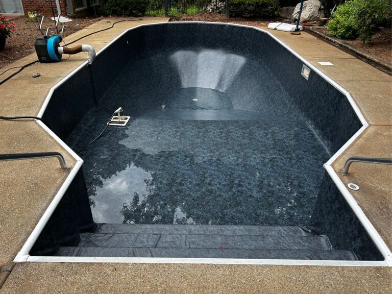 An empty, dark-patterned swimming pool under renovation with a sump pump on the concrete deck.