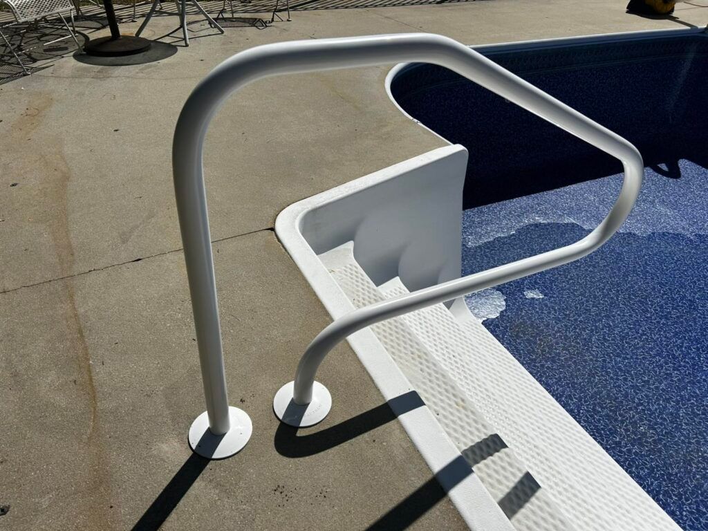 White metal pool handrail mounted on a concrete pool deck, providing support for entry into swimming pool steps.
